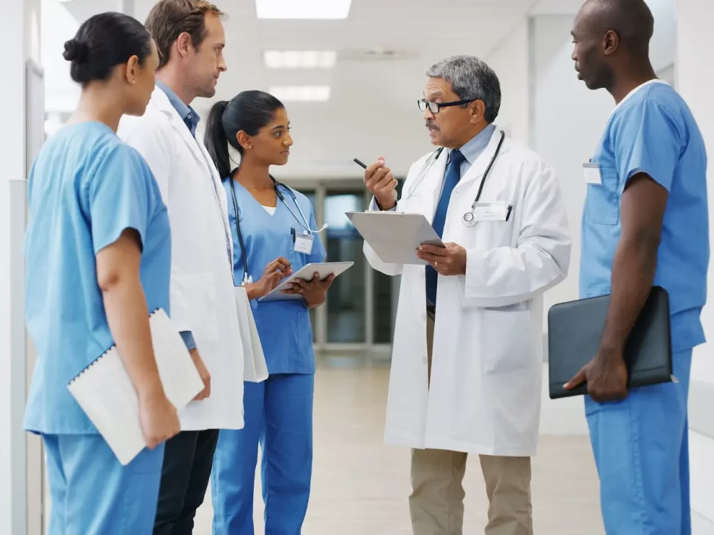 A group of healthcare professionals, including doctors and nurses, discussing patient care in a hospital hallway.