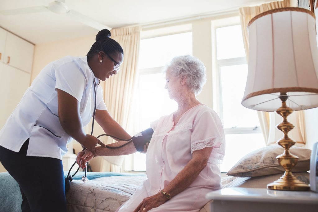 A nurse taking the blood pressure of an elderly woman in a cozy bedroom setting.