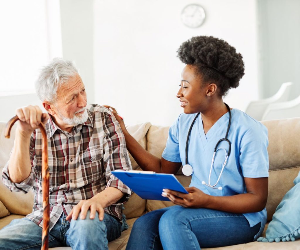 A caregiver speaking with an elderly man, offering support while holding a clipboard.