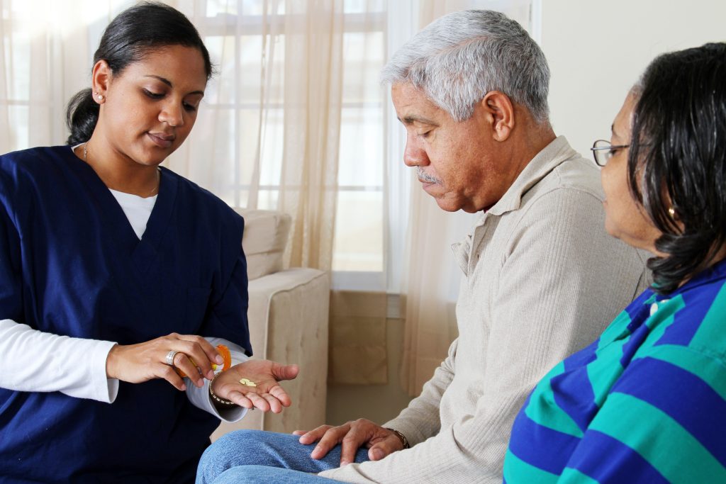 A nurse administering medication to an elderly man, while another elderly woman observes in a well-lit room.